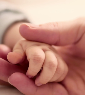 Parent gently holding newborn baby’s hand.